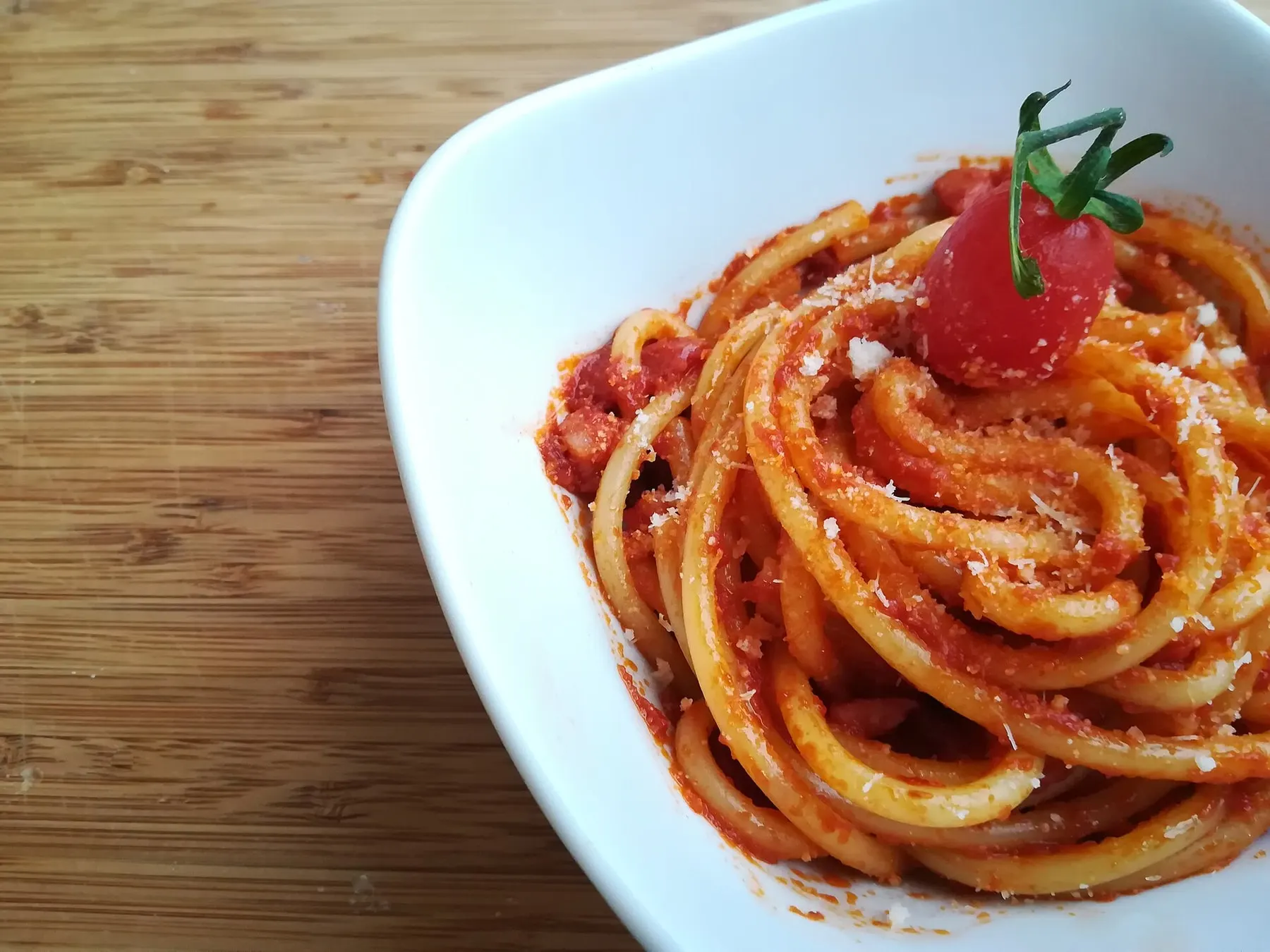 Bucatini all'amatriciana en un plato blanco, con pecorino rallado